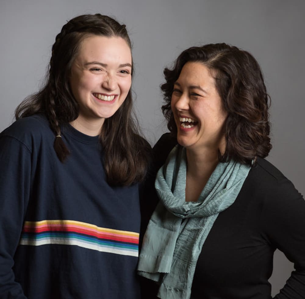 A woman and her daughter are standing together laughing.