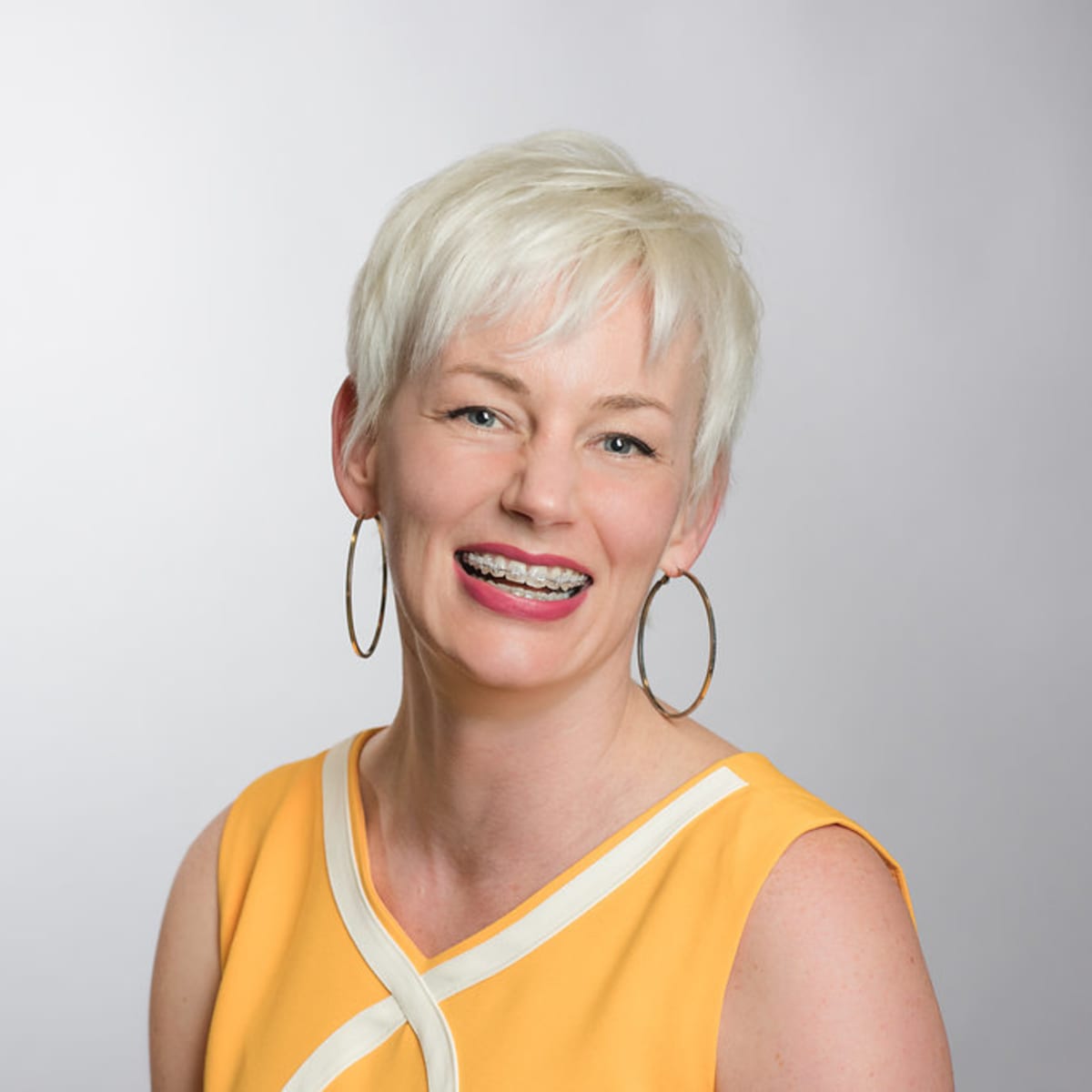 An older woman in a yellow dress smiles, showing off her braces.