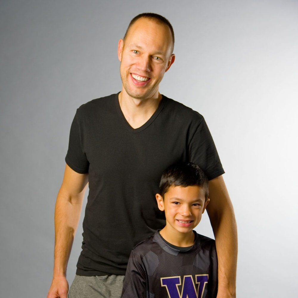 A father and son are standing beside each other smiling.