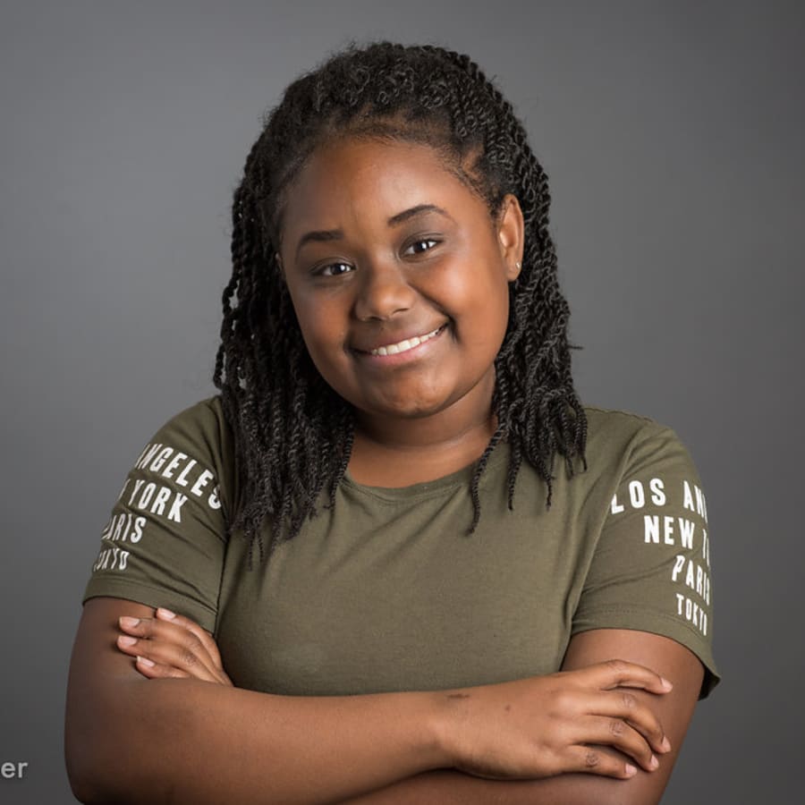 A woman standing with her arms crossed is smiling.