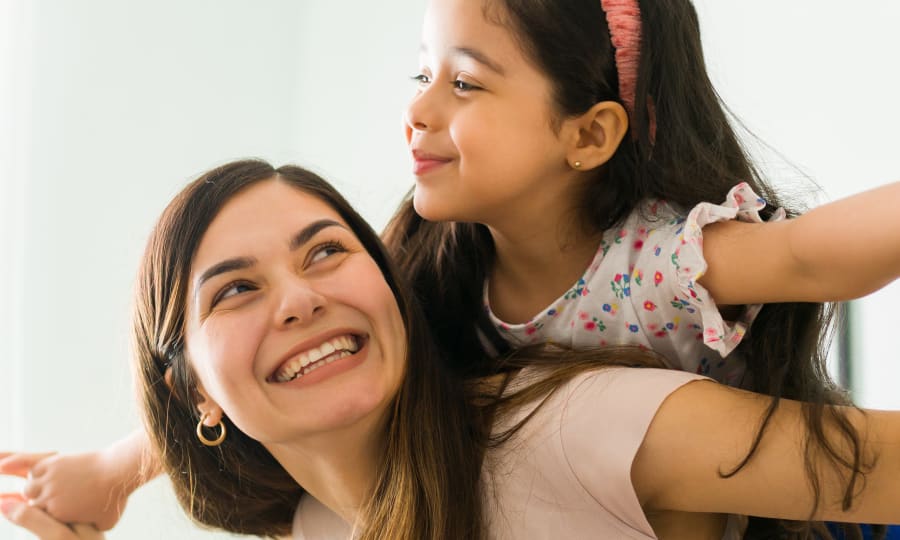 A woman smiles at a child she is carrying on her back.