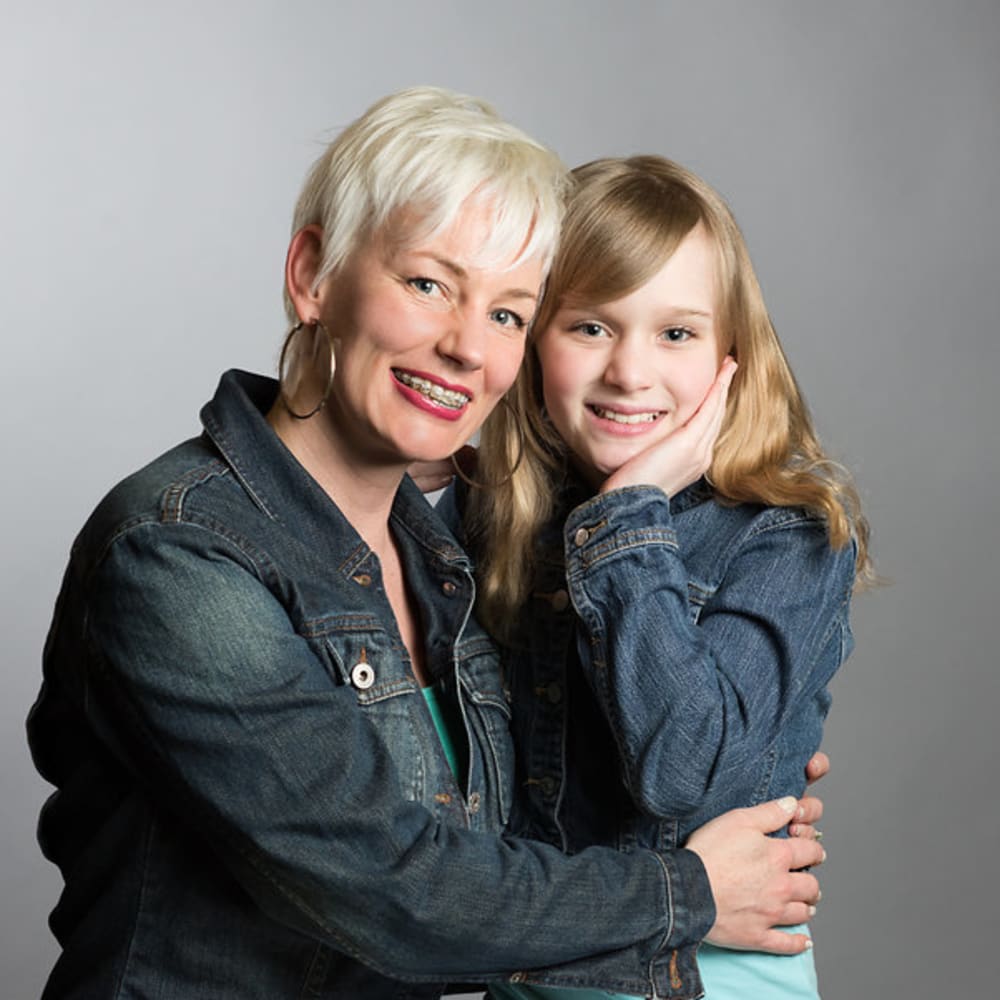 An older woman with braces is hugging her granddaughter. They're both smiling and wearing denim jackets.