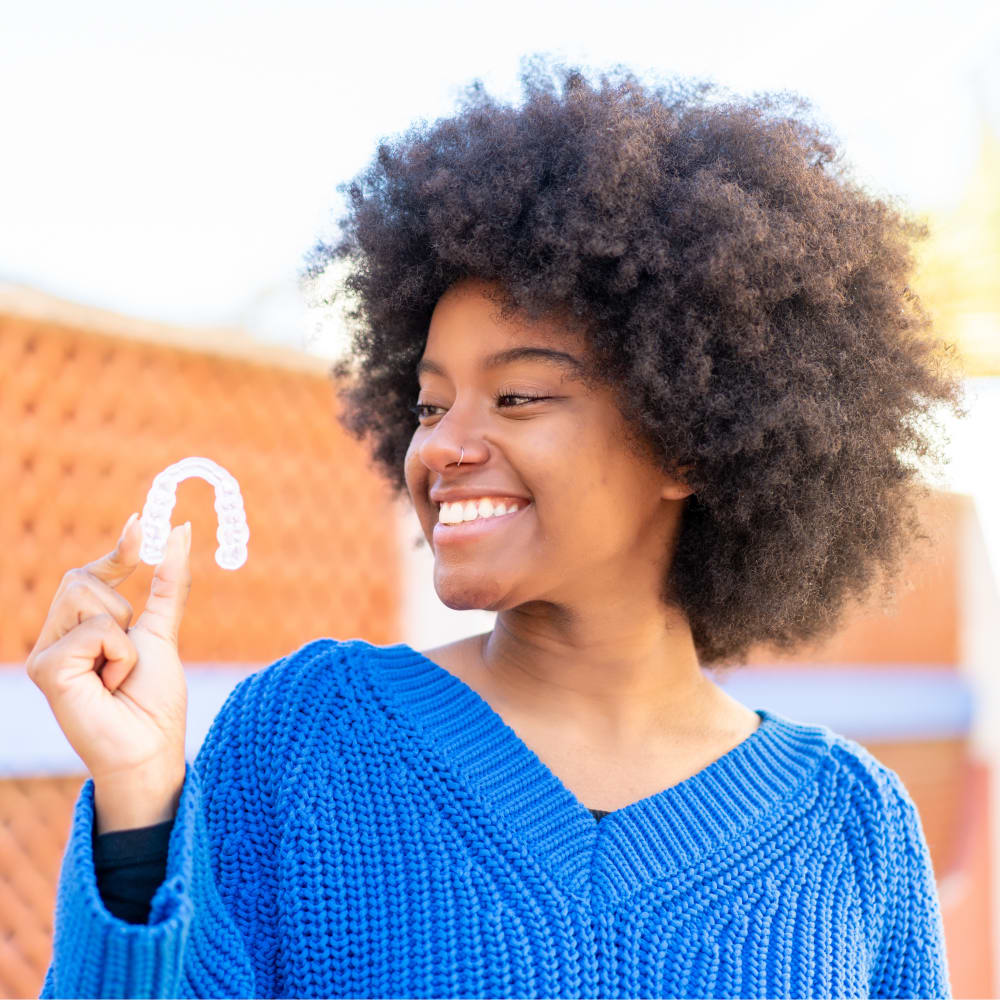 Smiling teenager looking sideways at the retainer she is holding.