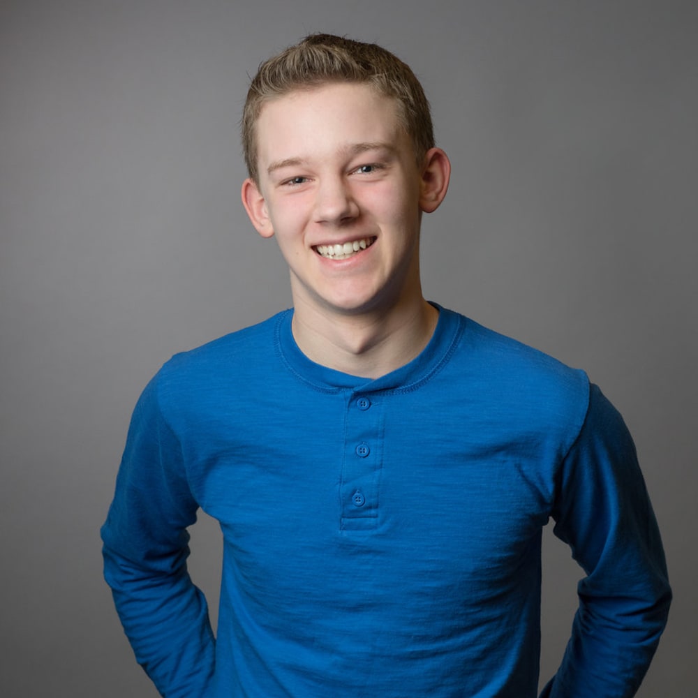 Teenage boy in a blue shirt is standing and smiling.